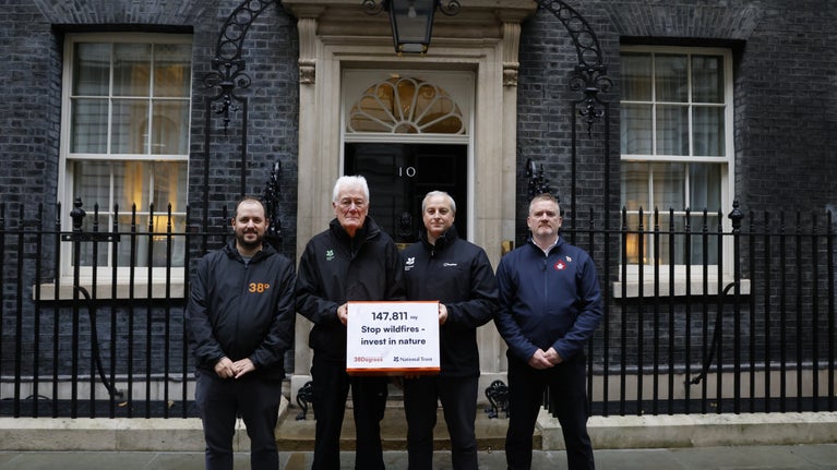 Four representatives from 38 degrees, National Trust and the Fire Brigades Union stand outside No. 10 Downing Street. They hold a sign that reads: 147,811 say Stop wildfires - invest in nature